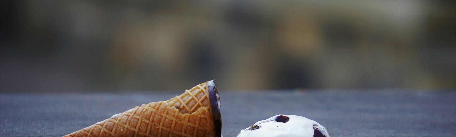 an ice cream cone laying on concrete, the ice cream next to it.