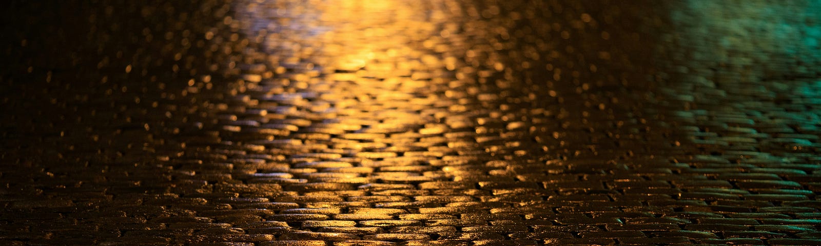 Wet paved road at night reflecting a golden hue from the streetlight.
