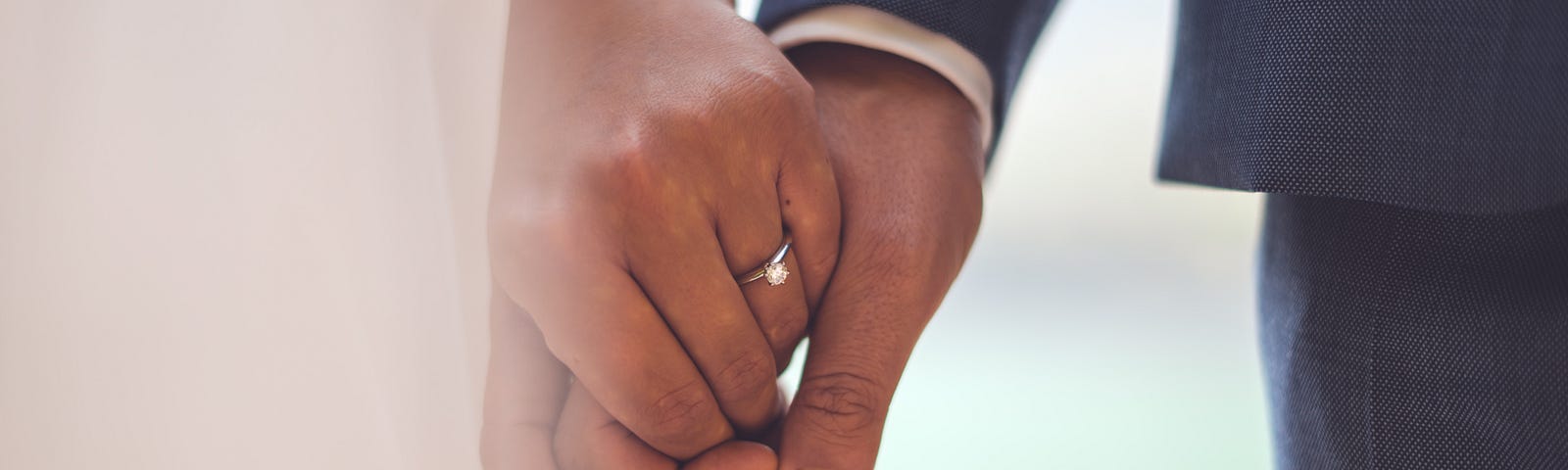 A close-up of a couple’s hands together, the woman in a white dress and the man in a suit.