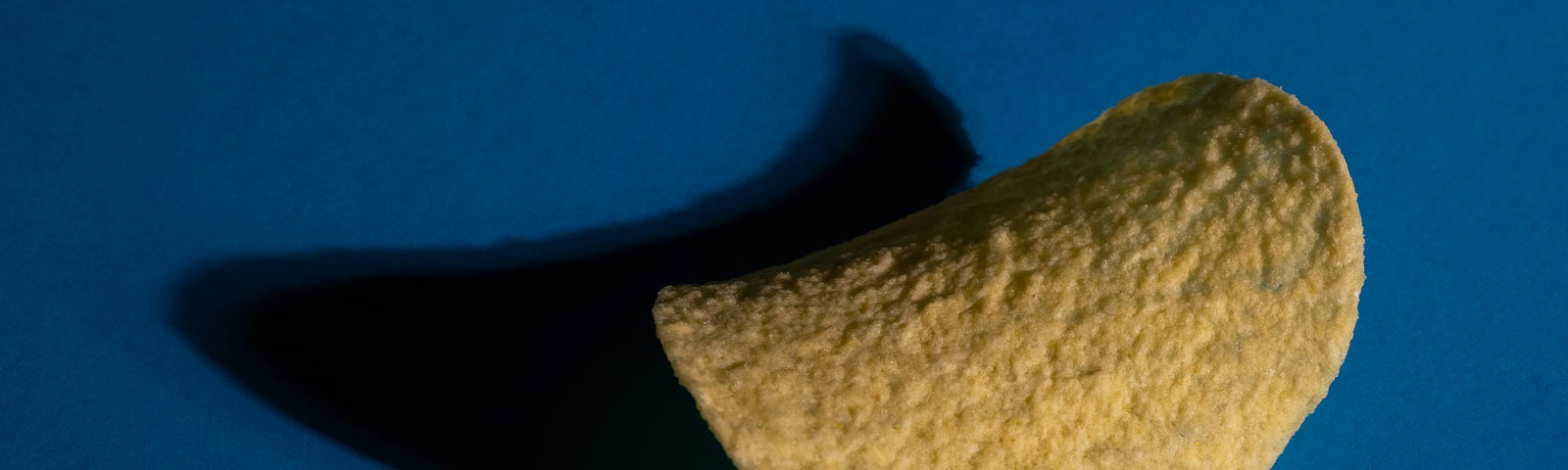 A single Pringles potato chip, a highly processed food. Dark blue background.