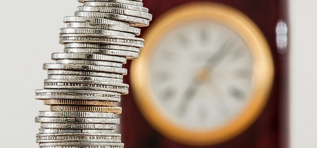 Une pile de pièces devant une horloge symbolisant que le temps c’est de l’argent