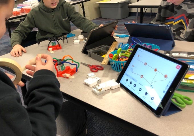 Two students gathered around a table to collaborate on a SAM Labs project. Items include a table with SAM Studio features, pipe cleaners, SAM blocks, and other craft materials.