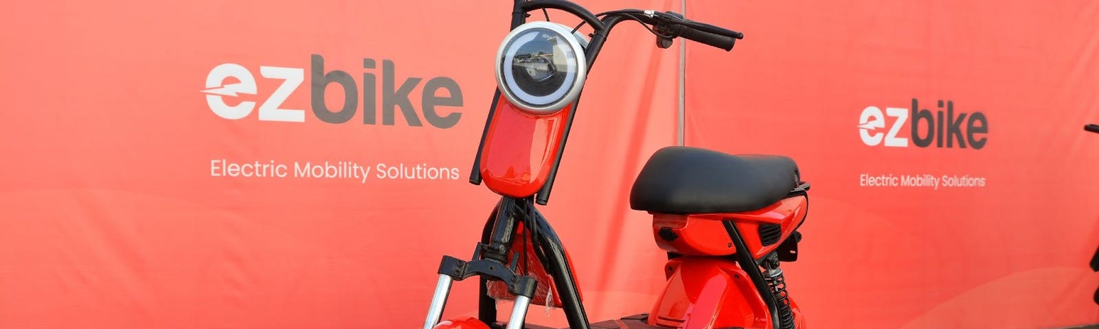 An orange electric motorbike in front of sign saying ezBike