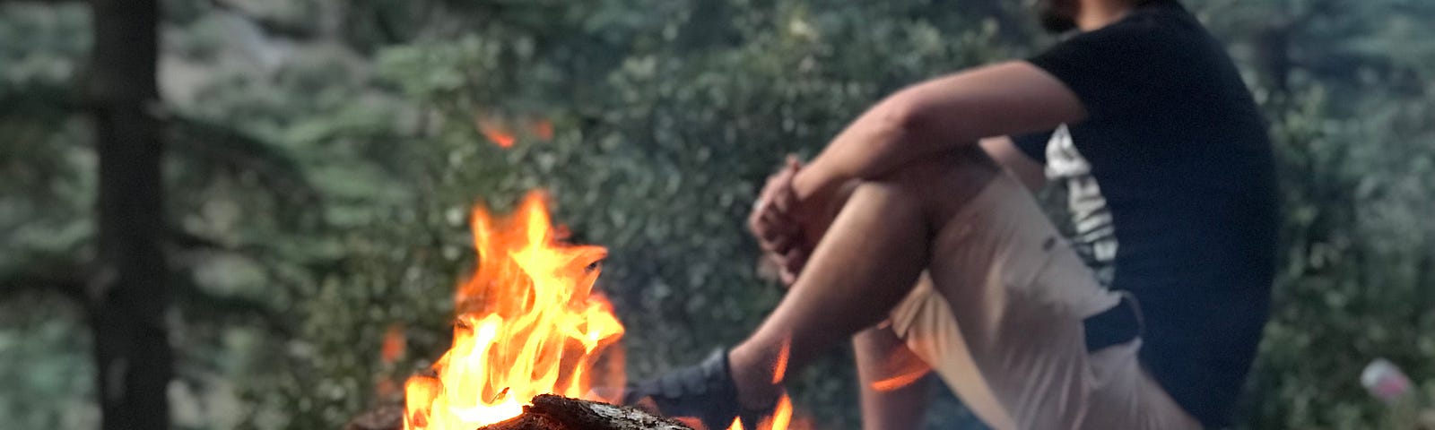 A man sitting next to fire in the forest