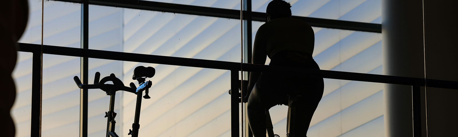 A person riding a spin bike for exercise in a gym while looking out the window.