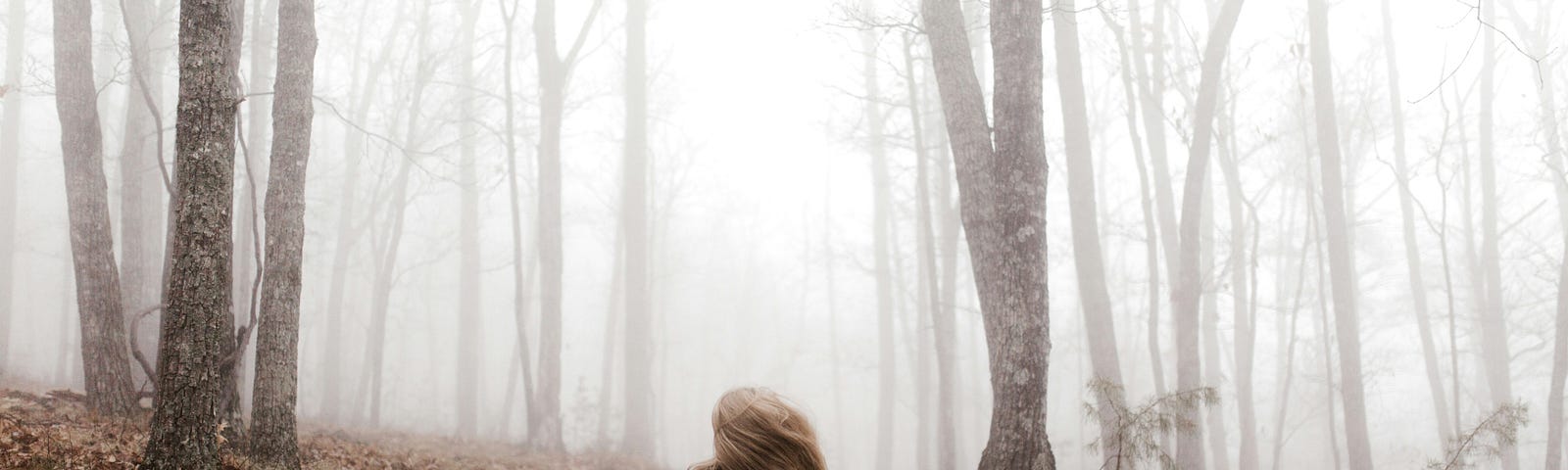 Person sitting on a misty forest path, reflecting and surrounded by bare trees, symbolizing introspection and the unknown.