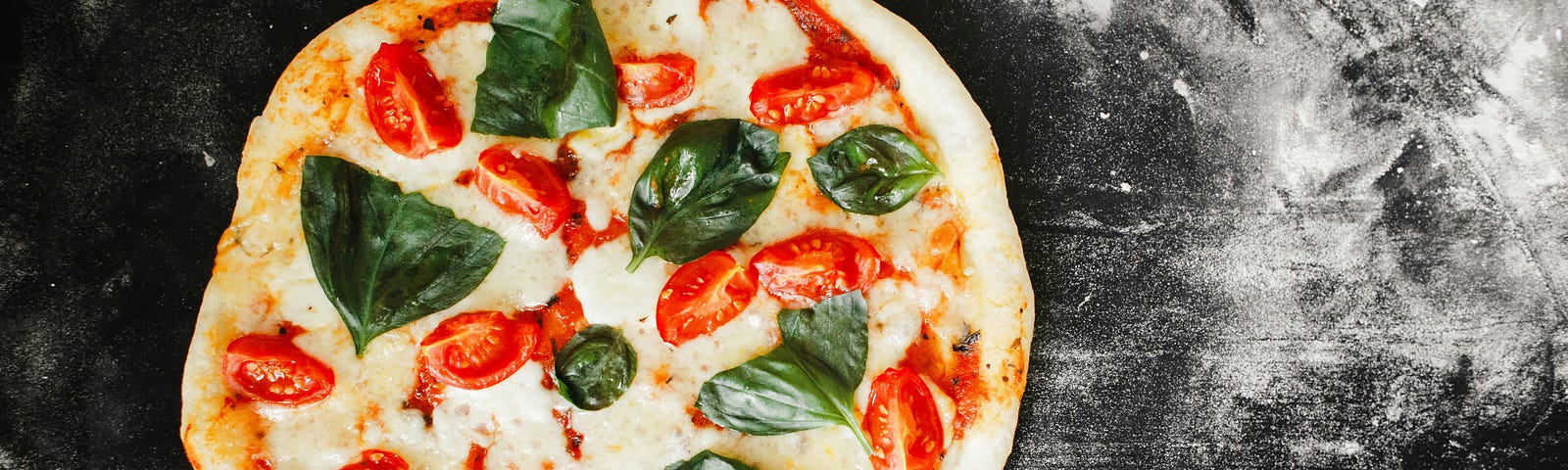 A pizza with sliced tomatoes and basil on a dusted black countertop