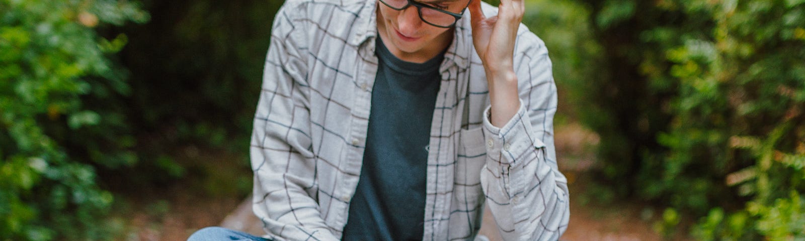 young man sitting cross legged outside reading a book