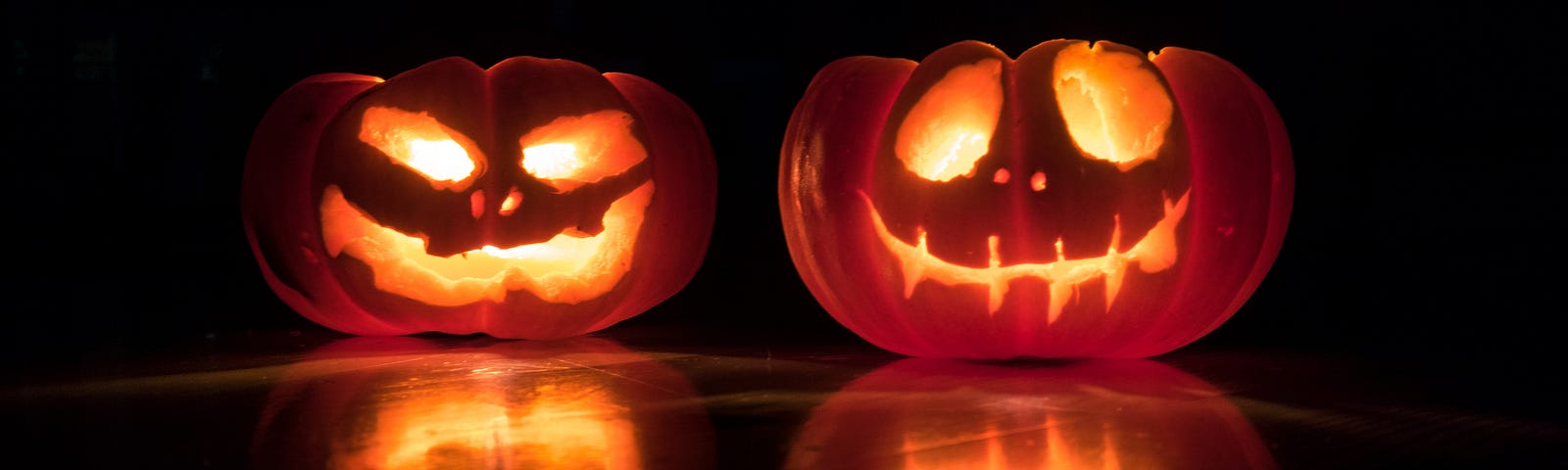 Two pumpkins carved with faces and lit with candles