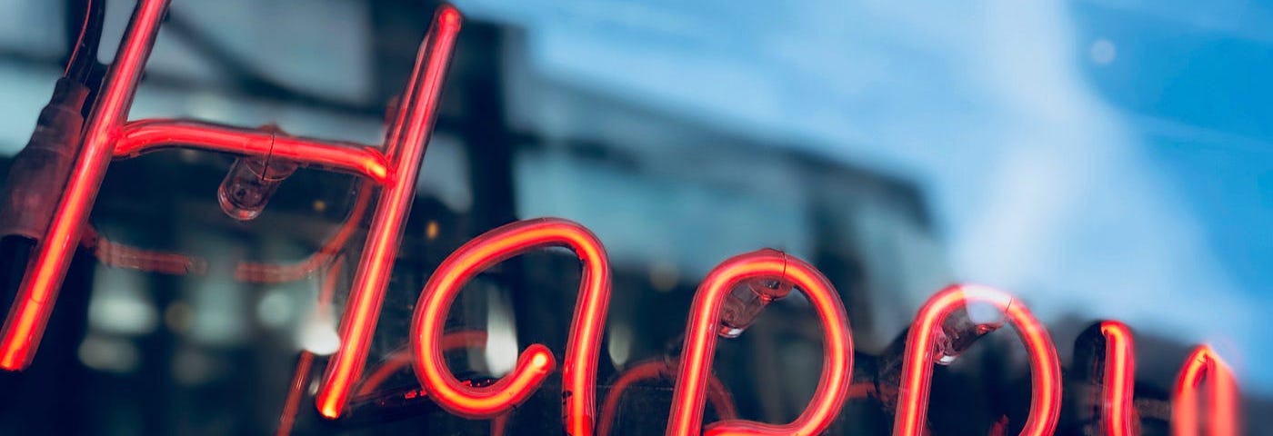 A neon sign with the work Happy in red letters against a dusk background.