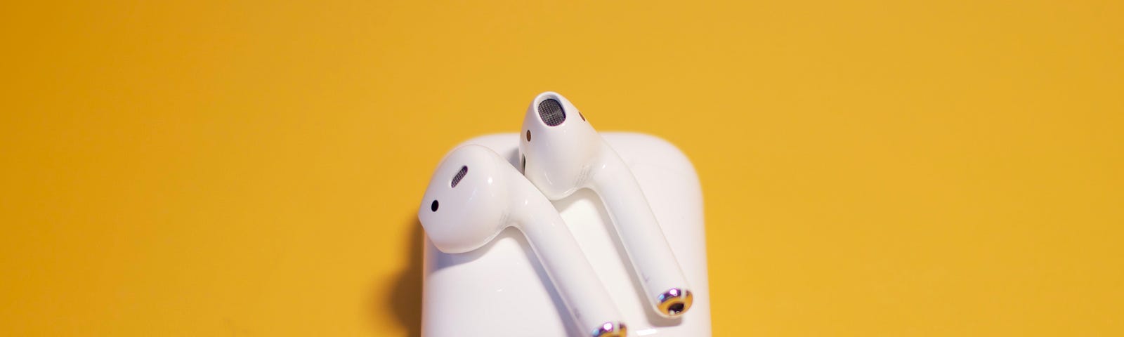 AirPods lying on the case on a yellowish backgrund.