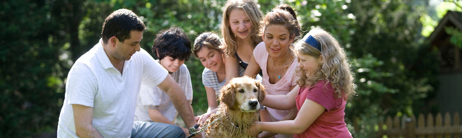 A family giving their golden retriever a bath in the garden.