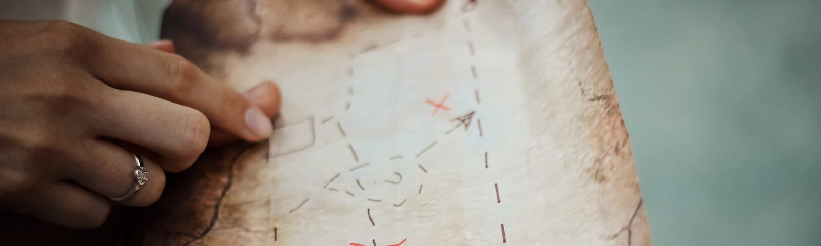 Two sets of hands holding a hand drawn treasure map. One of the hands is pointing to a position on the map.