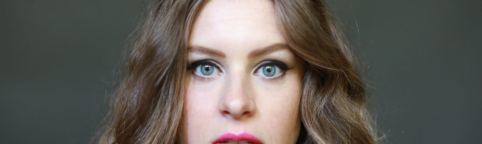 This image shows a person from the shoulders up, looking straight at the camera with slightly open mouth. The person has long, curly hair and has a slight frazzled look.