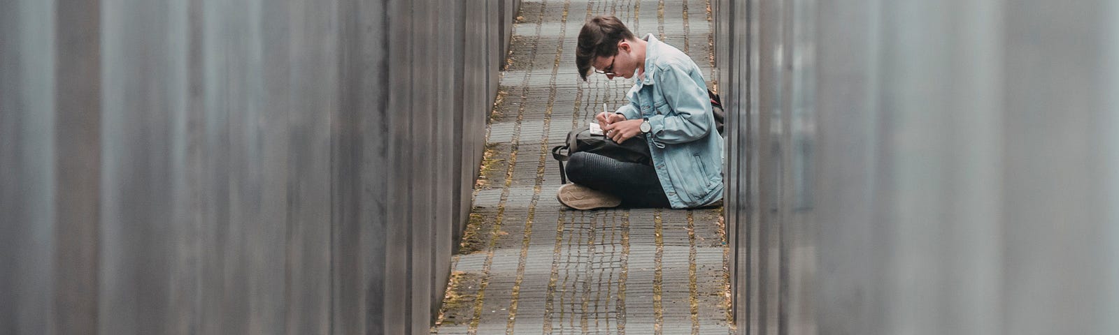 A person sitting in a narrow pathway while writing.