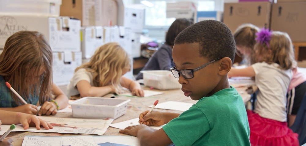 I picture of elementary age students working in a classroom with an African American child in a green shirt in the foreground.
