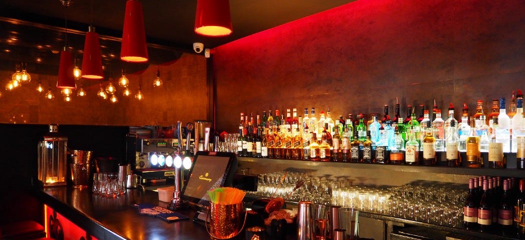 A photo of a bar with bottles of alcohol lined up against the wall.