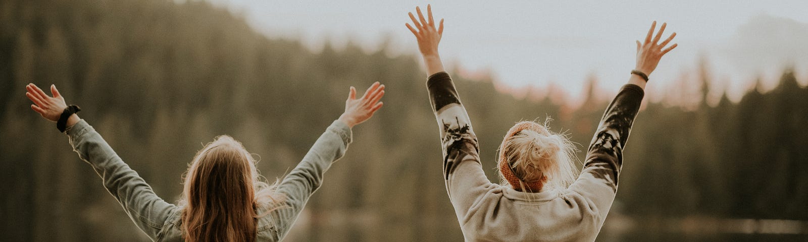 Two women facing a small body of water with their hands in the air in celebration.