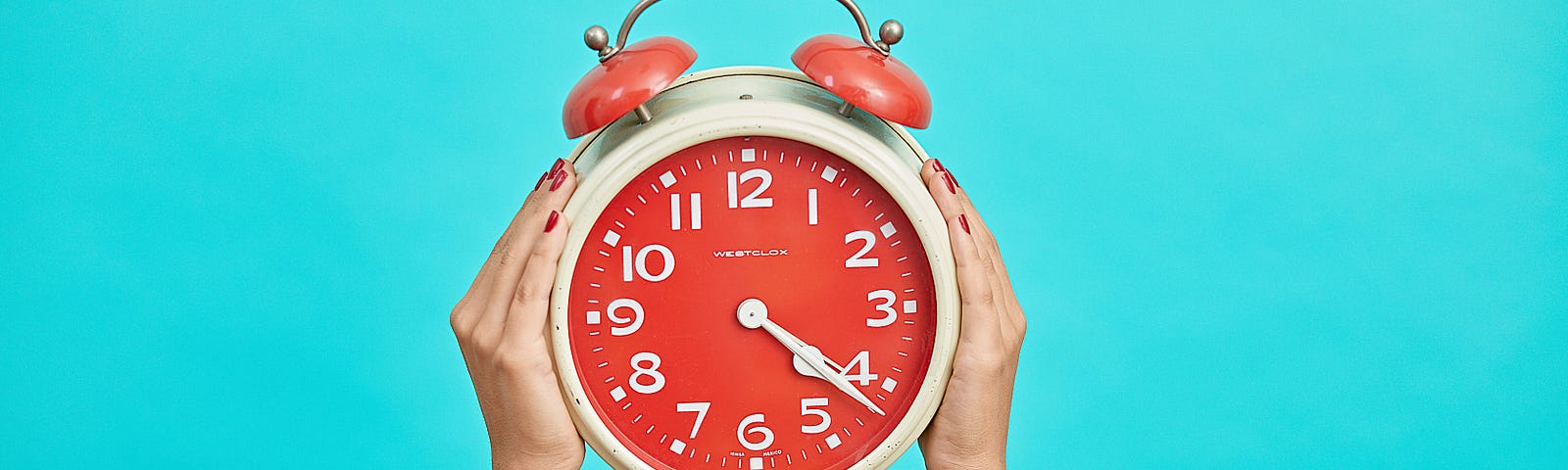 A person’s arms extend upwards, holding an old-fashioned alarm clock (with a red face and two red bells on top). Power blue (Tiffany) background.