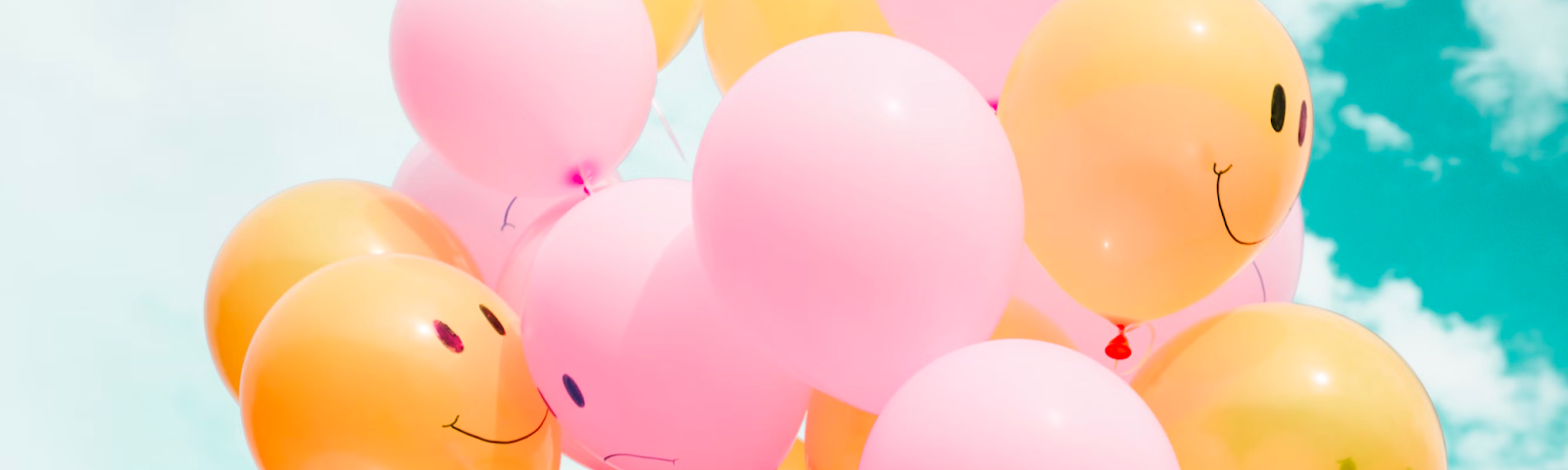 Shown is a group of pink and yellow balloons. The pink balloons have a sad face on them and the yellow balloons have a happy face.