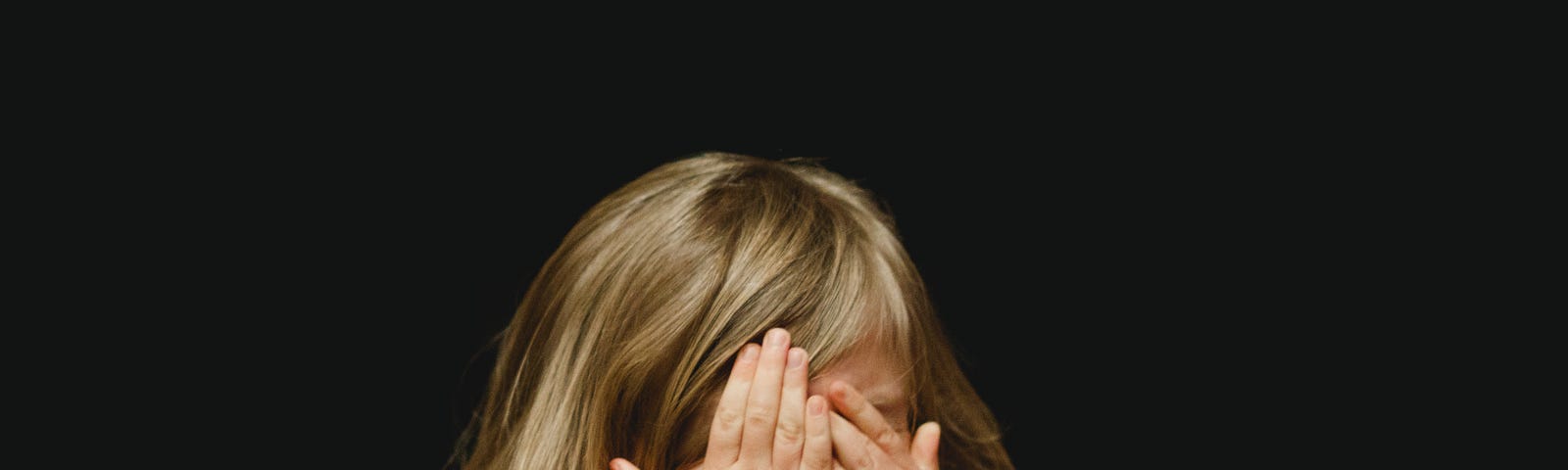 A young girl hiding her face behind her hands as if ashamed.