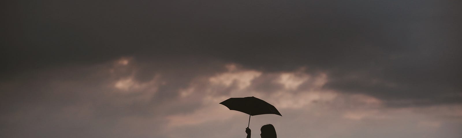 A picture of a dark stormy sky and two people sharing an umbrella.