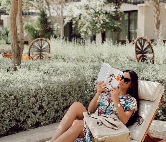 Woman reading a book while sitting on a chaise lounge outdoors