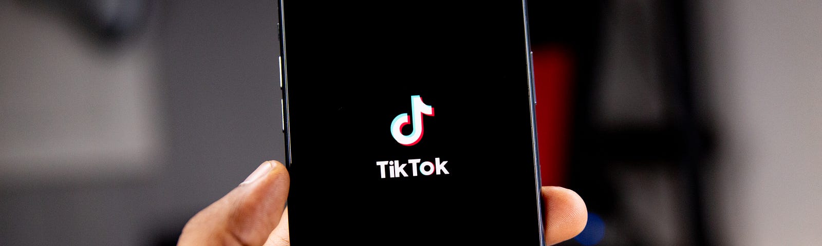 A left hand holding a smartphone with a black screen expect for the TikTok logo in the middle as the app loads.