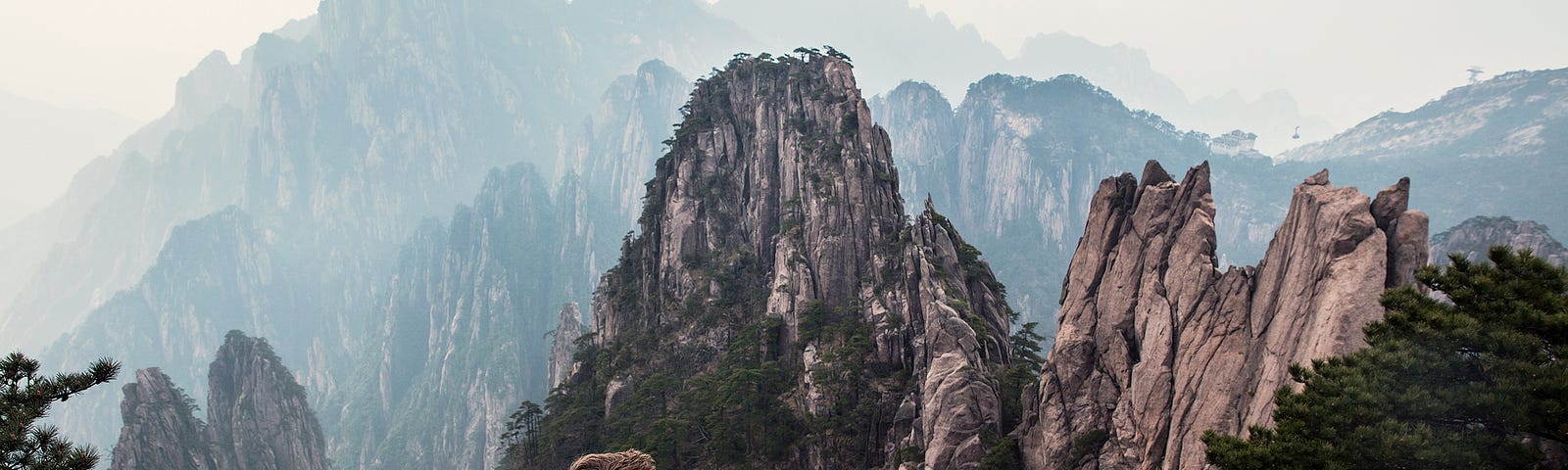 Man sitting on rock, gazing at mountains in the distance.