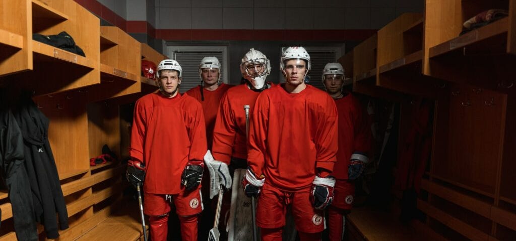 Five somber looking hockey players standing in an empty locker room. Image courtesy of Tima Miroshnichenko at Pexels.