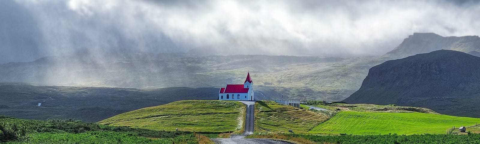 A gravel road leading to a church in the distance landscape. A storm is brewing.