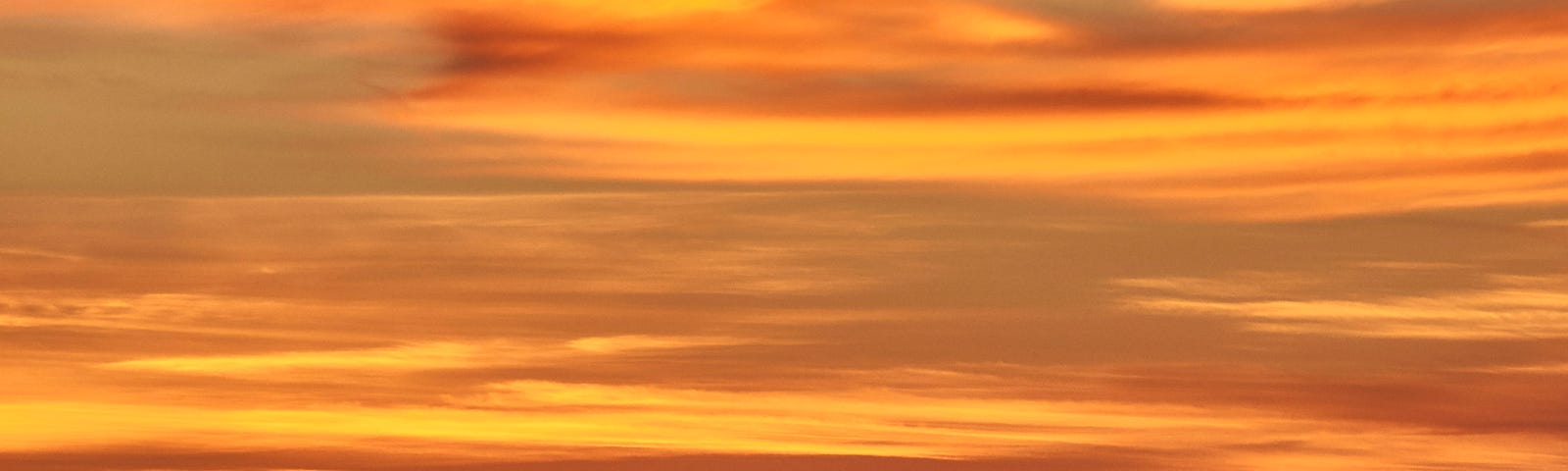 A cargo ship passes along the horizon during a dusk with a rich orange sky