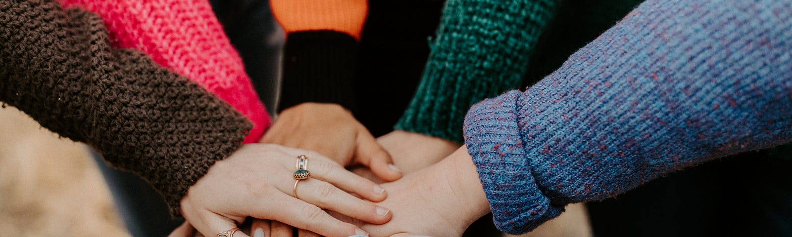 Several hands with various coloured sleeves coming together in the centre of a circle.