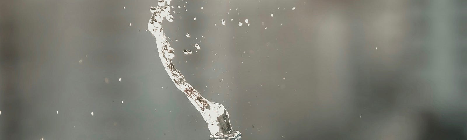 A person squeezes a plastic bottle of water, causing the fluid to spurt upwards.