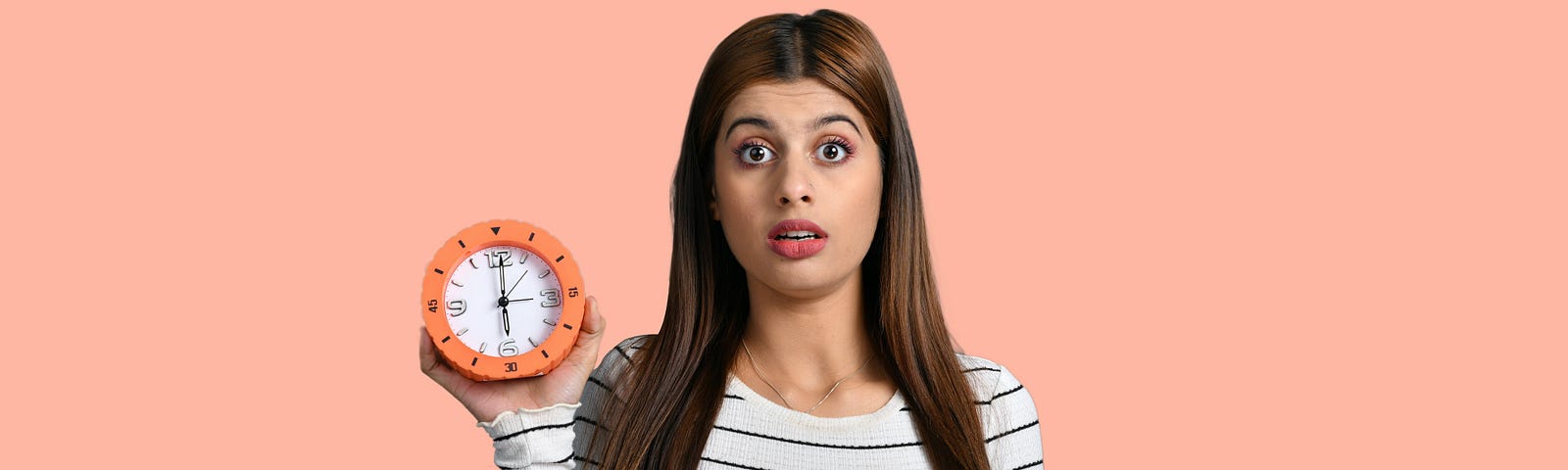 Lady holding a clock timer in her hand. She has long brown hair and is wearing a long-sleeved white stripey top.