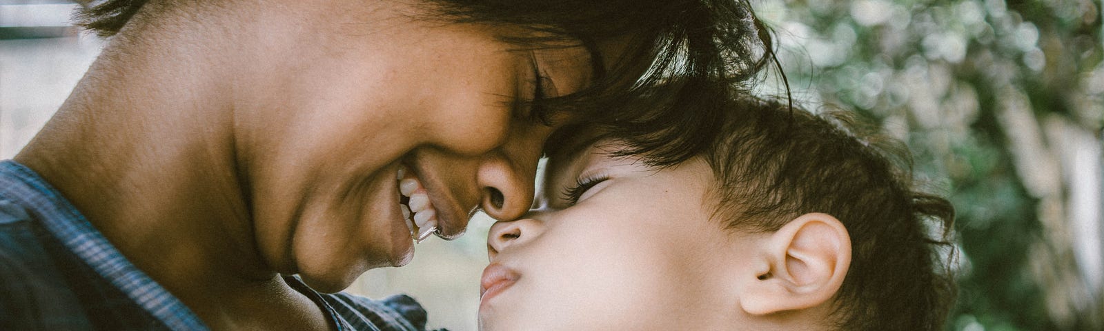 Picture of smiling woman nuzzling noses with a young boy.