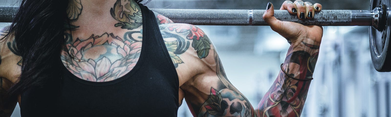 A tattooed women has a barbell on her back/shoulders. Cardiovascular exercise and strength training are two of my pillars of fitness, each claiming the throne in the kingdom of longevity.