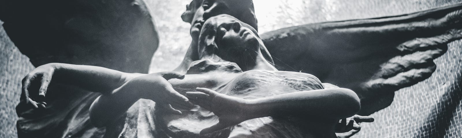 Stone statue of an angel lifting a woman up and away.