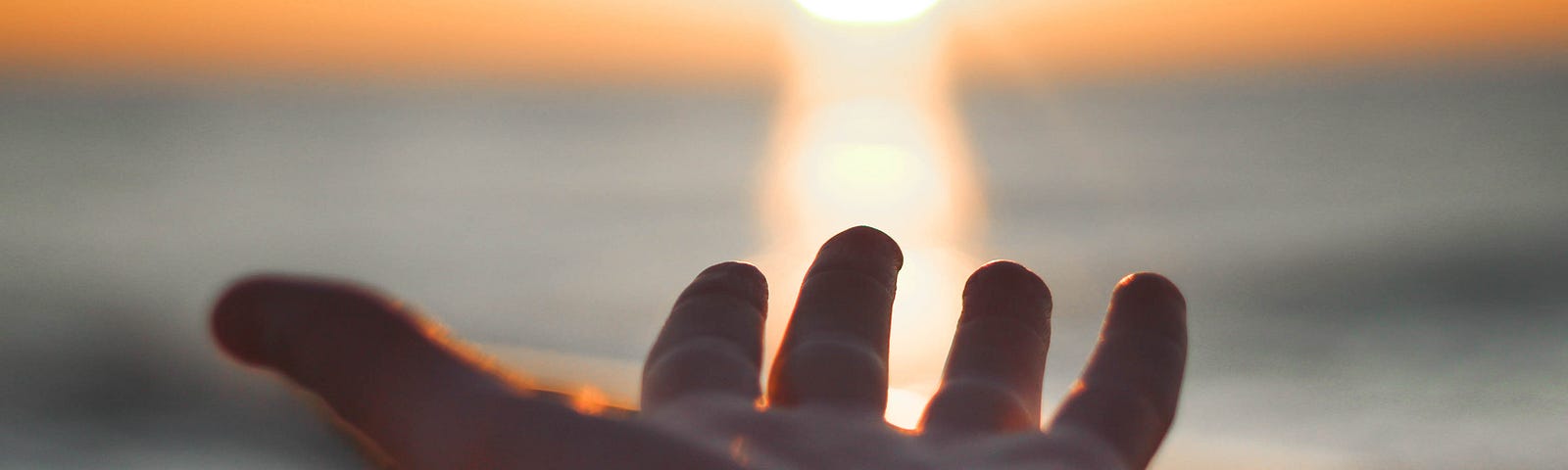 An outstretched arm reaches out for the setting sun in the distance. The background is blurred. Ultraviolet radiation exposure is the leading cause of skin cancer, including melanoma.