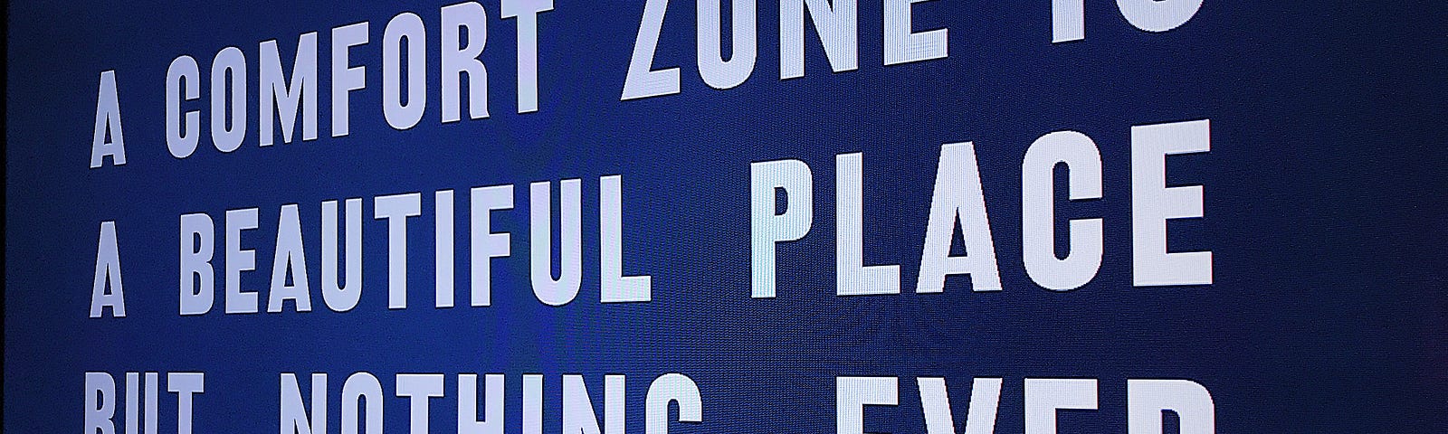 A blue interactive board reads “A comfort zone is a beautiful place but nothing ever grows here” in white all-caps.