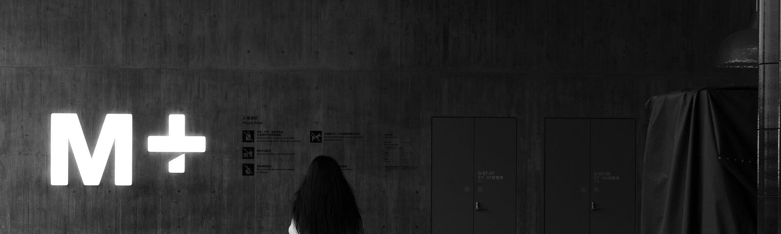 A person walks through a large empty room toward a glowing M+ on the wall, Roman Numeral for 1,000.