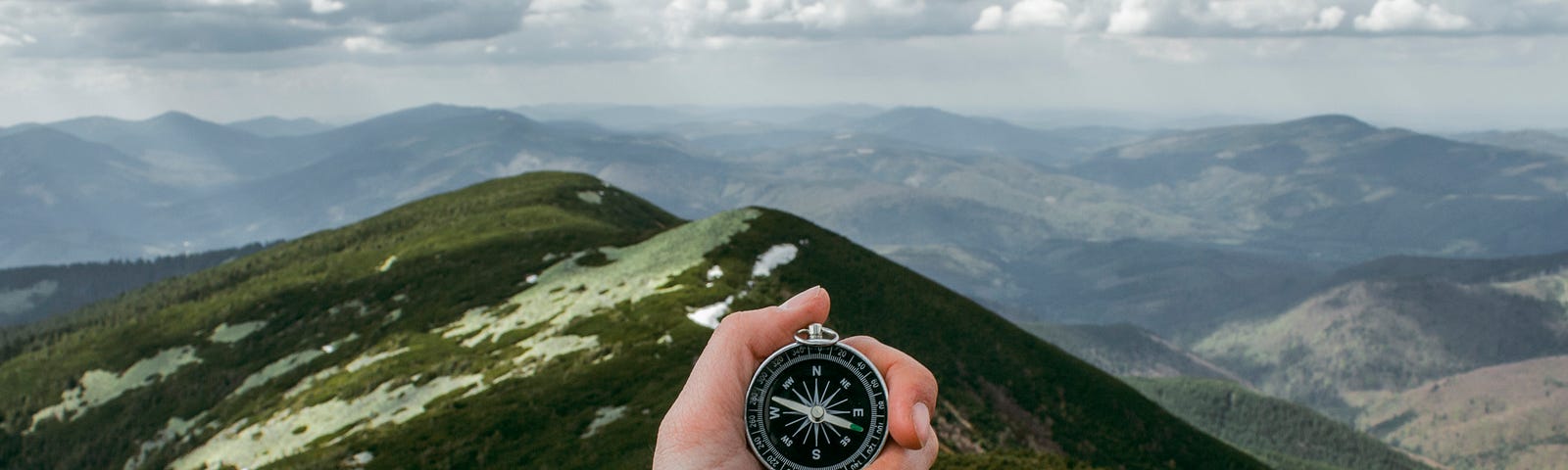 Man standing up in the mountains and holding a compass in his hands