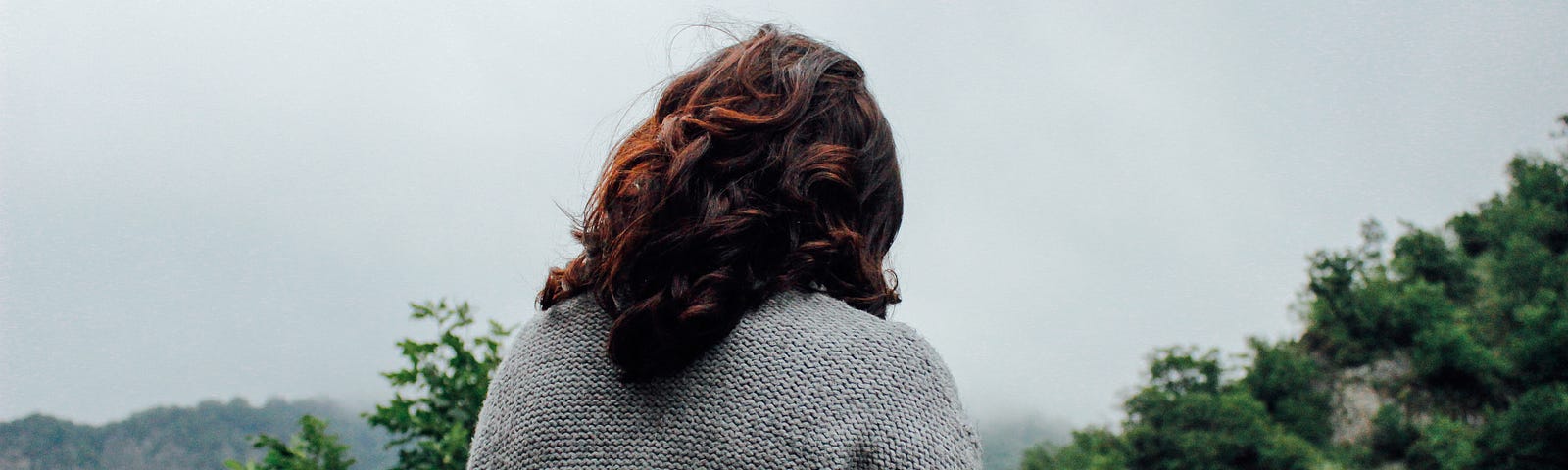 A woman outdoors with her back turned and wearing a heavy sweater