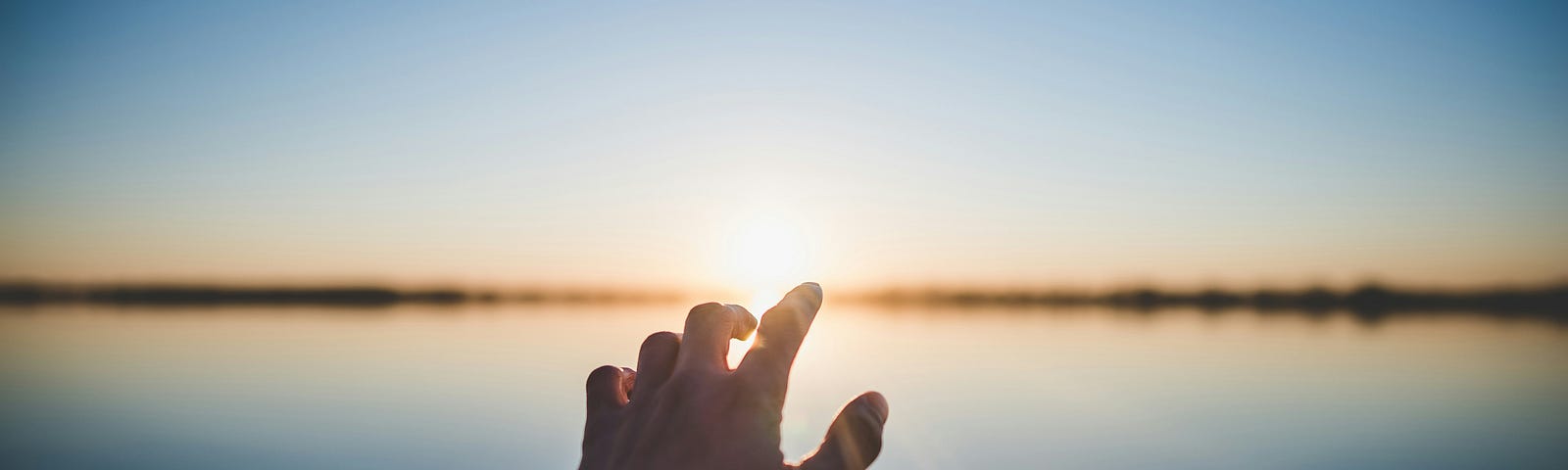 Man’s hand reaching toward sunrise on smooth lake