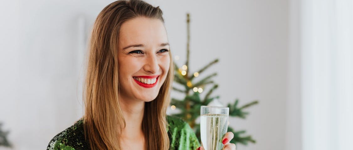 A lady with a lovely smile in a green dress is holding a wine glass in her left hand. Photo by Karolina Grabowska on Pexels.