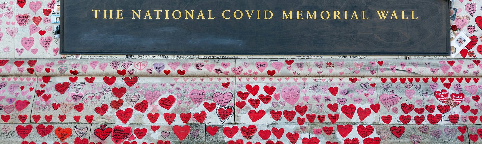 The National covid memorial wall with hearts, names and a few photos above the plaque.