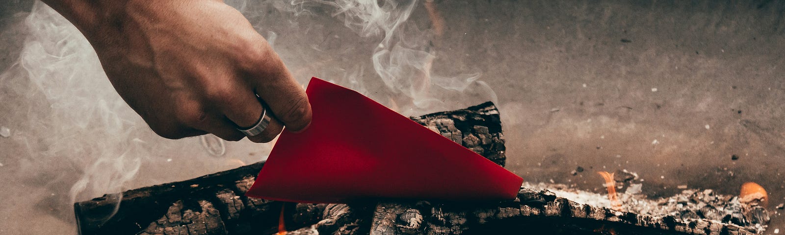 a hand putting a piece of paper into a lit fire.
