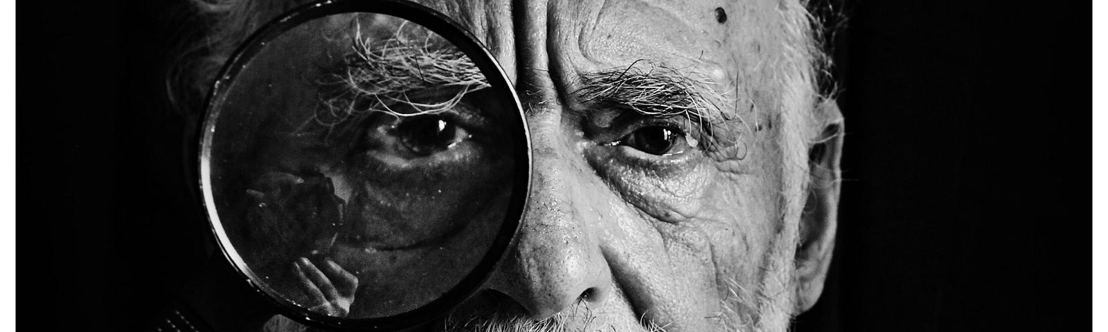 Black and white photograph of an old man looking towards the camera through a magnifying glass