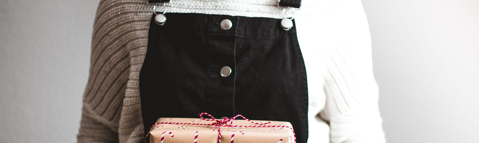 Woman in overalls and a sweater holding a Christmas gift box.