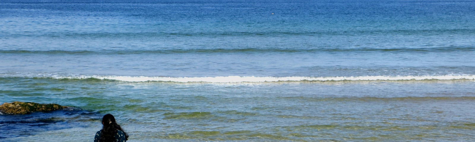 woman looks out at the sea. Appears to be an older woman wearing a blue and white gown. Wistful tone.